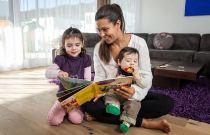 Ein Betreuerin von Kinderbetreuung zu Hause liest zwei Kleinkindern ein Buch vor. 